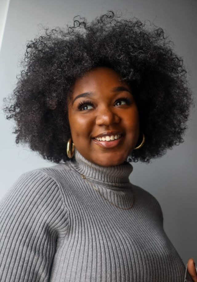 A portrait of Destiny Kearney, a person with long black curly hair and a gray shirt.