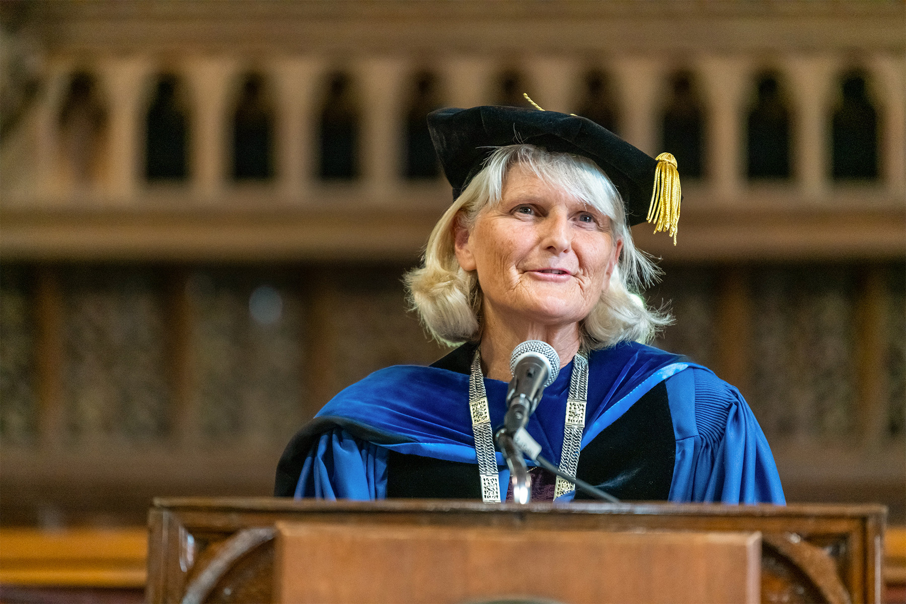 Pictured: Elizabeth pradley. A person in a graduation cap and gown standing at a podium speaking.