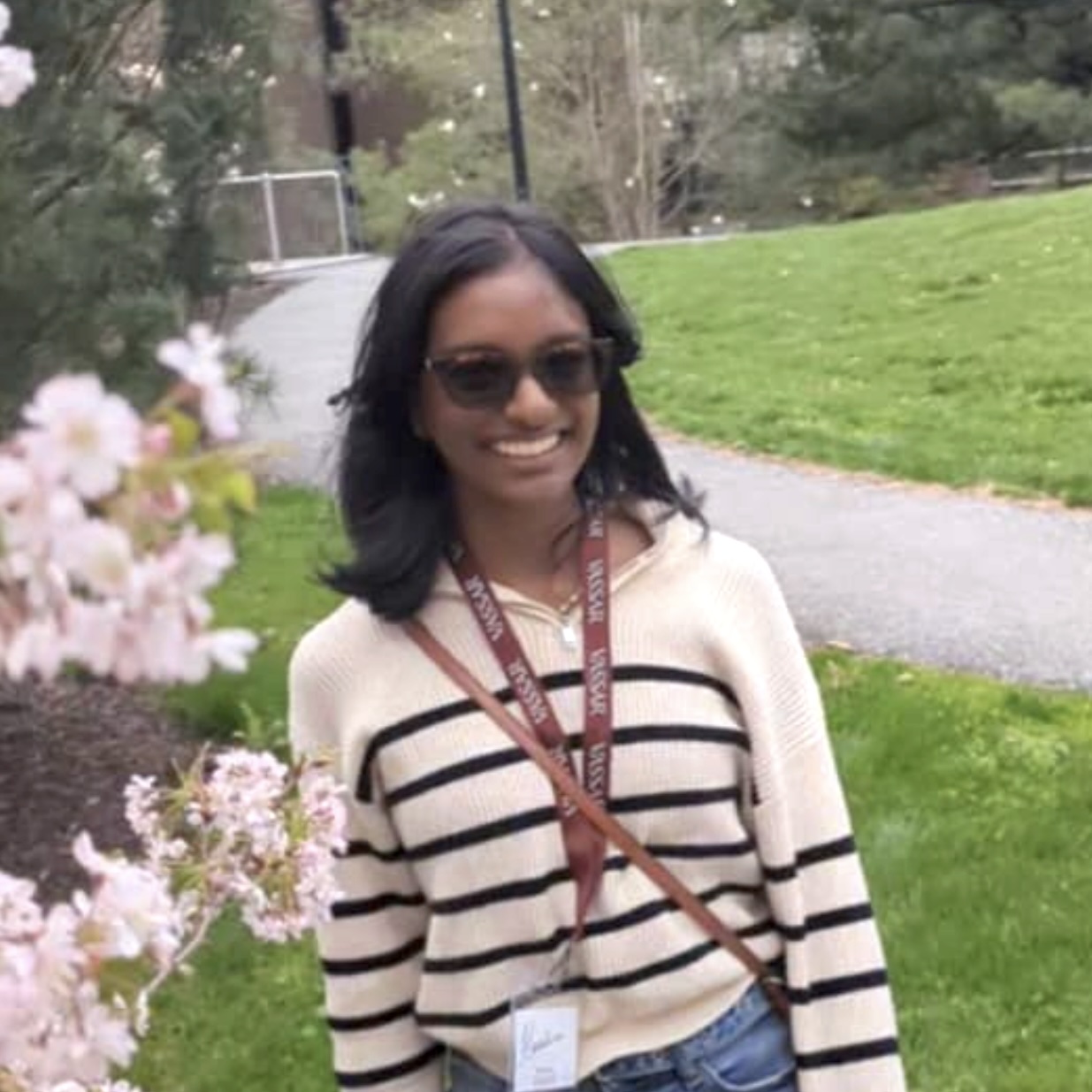 A headshot of Harshini Pothuganti, a person with long black hair, sunglasses, and a beige shirt with black stripes.