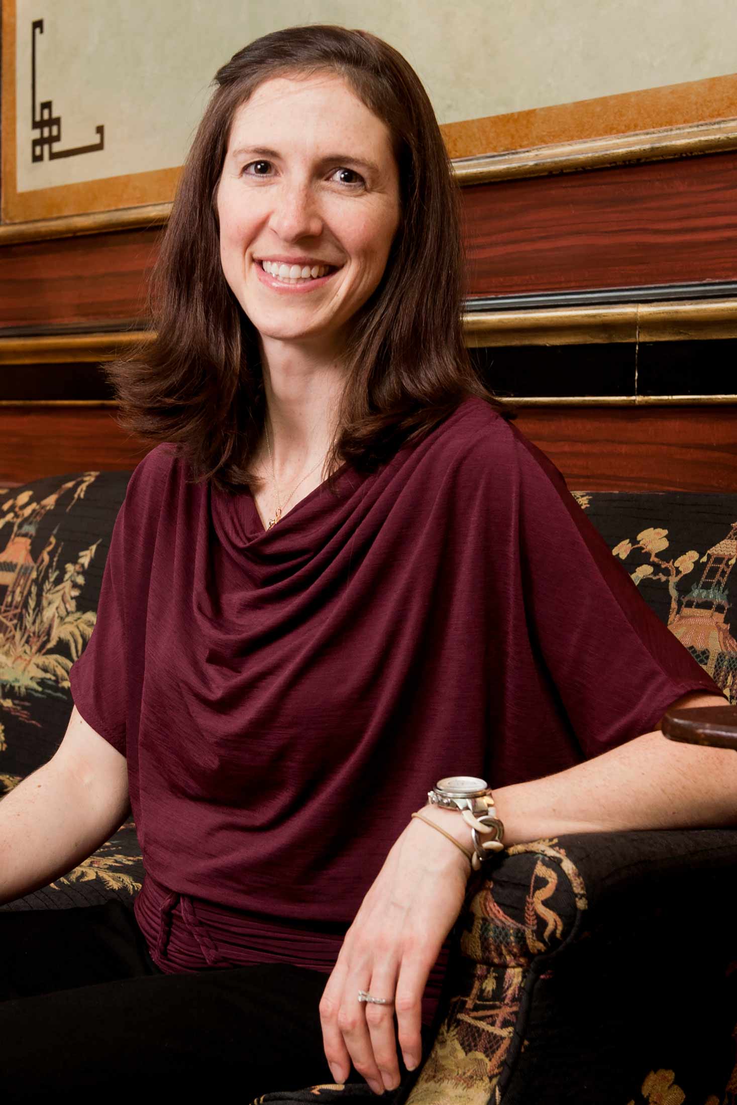 A photo of Leah Bendavid sitting on a couch and smiling toward the camera.