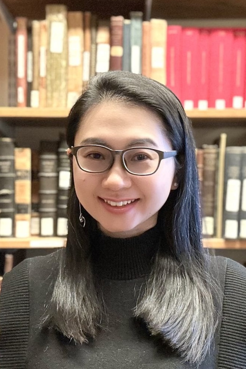 Person with long dark hair and glasses smiling in front of a book case.