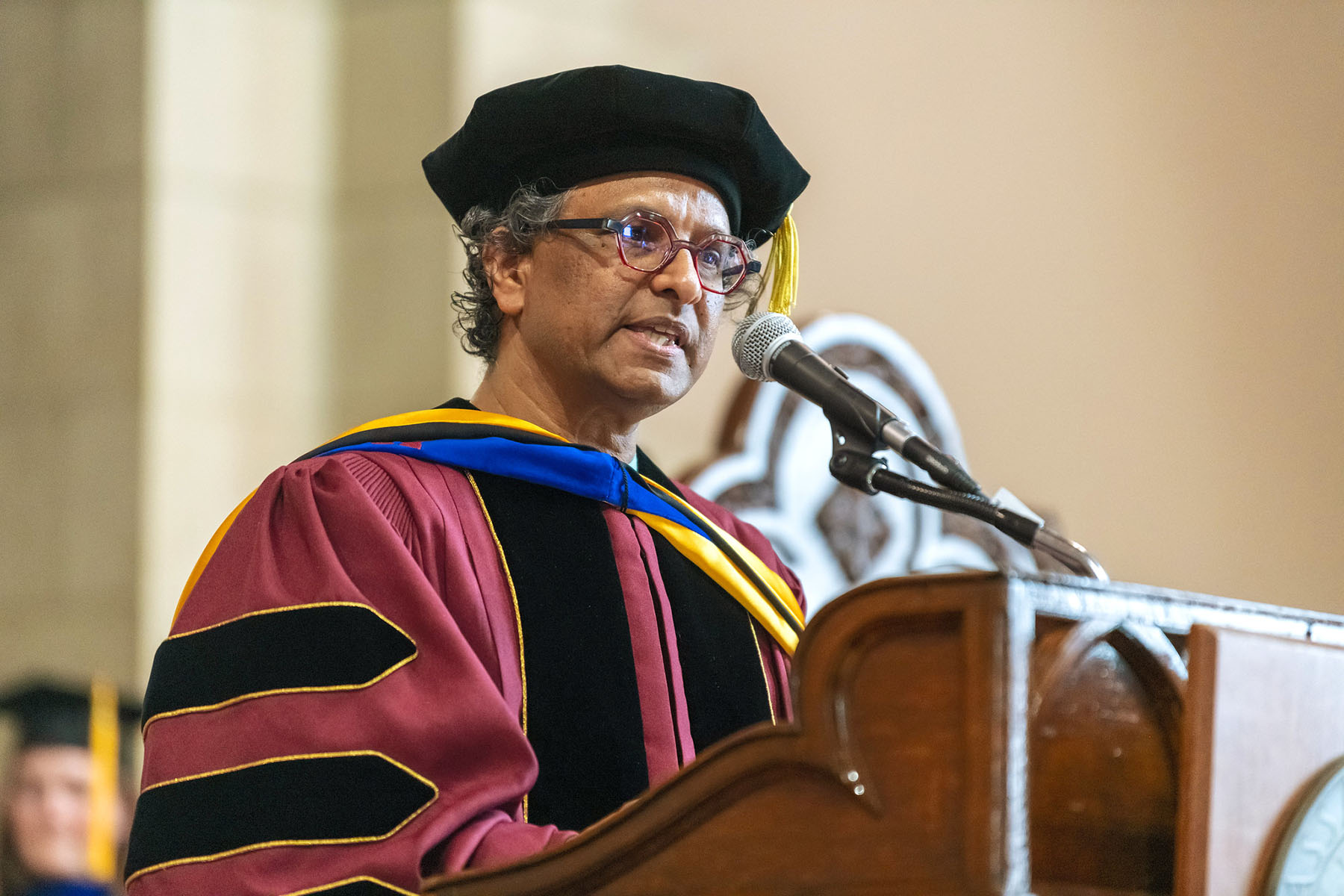 Pictured: Elizabeth pradley. A person in a graduation cap and gown standing at a podium speaking. to an audience.