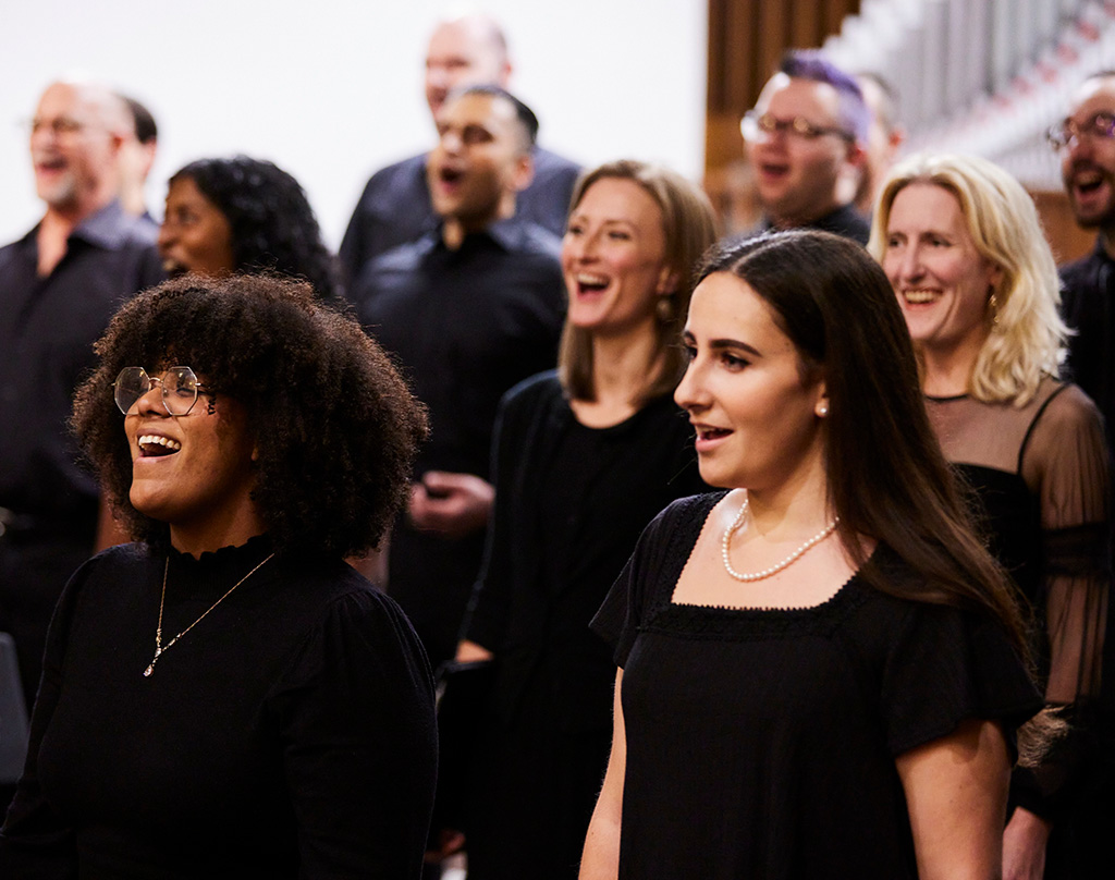 Close-up of a choir, eight members singing in a concert, all wearing black