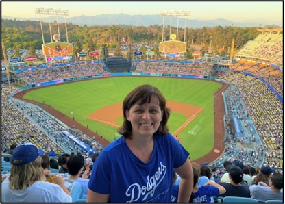 Person standing in a baseball stadium with the field in the background.