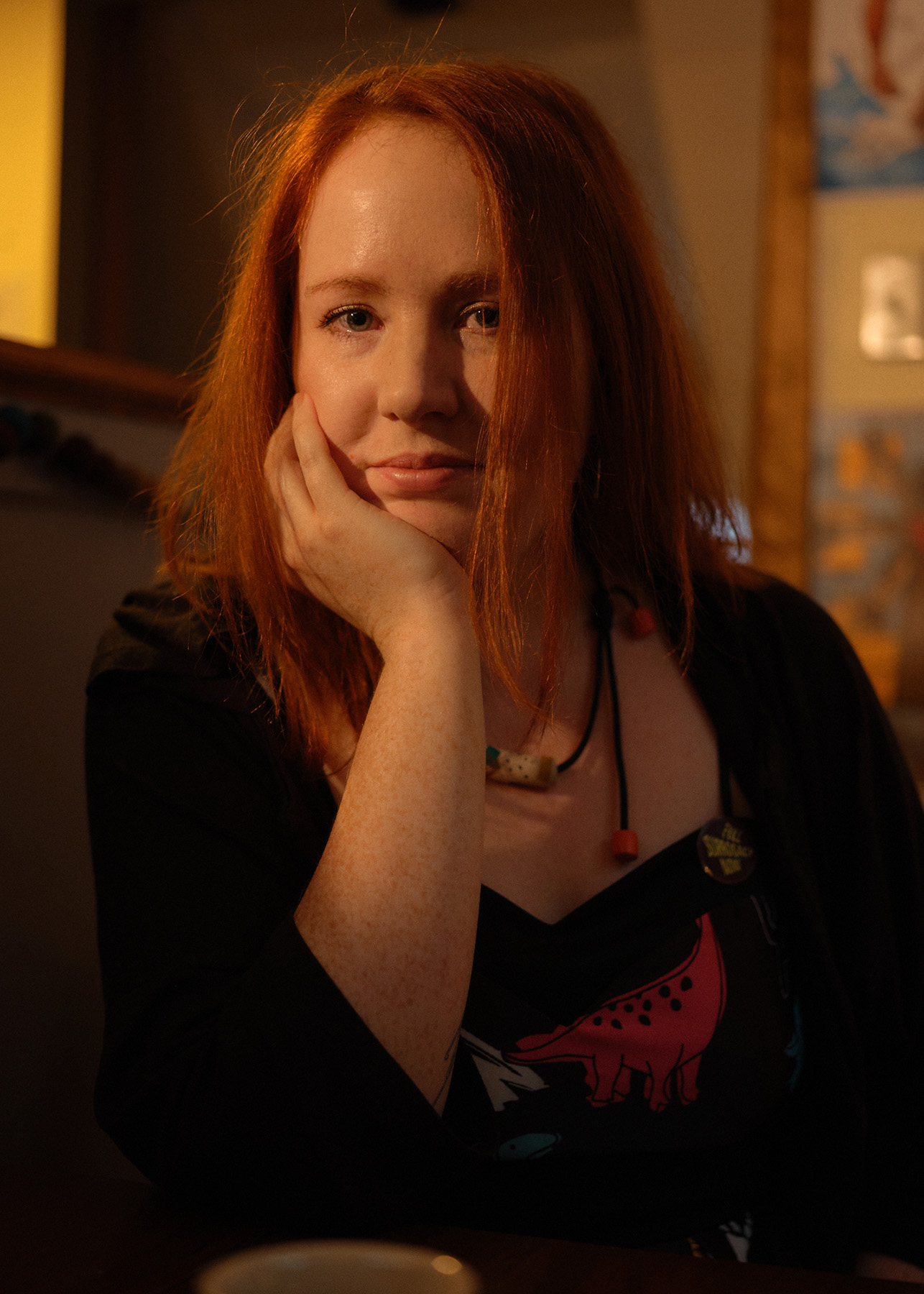 Person sitting in a dark room with long red hair resting their chin on their palm.