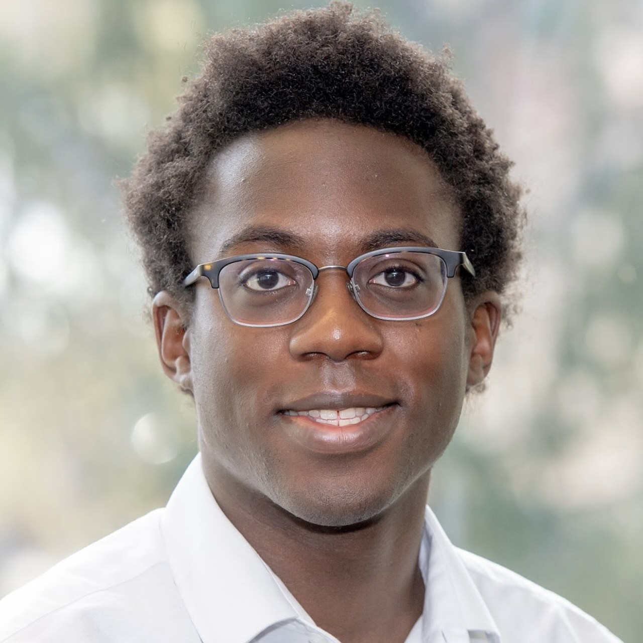 A headshot of Zephan Aruede, a person with short black curly hair, glasses, and a white shirt.