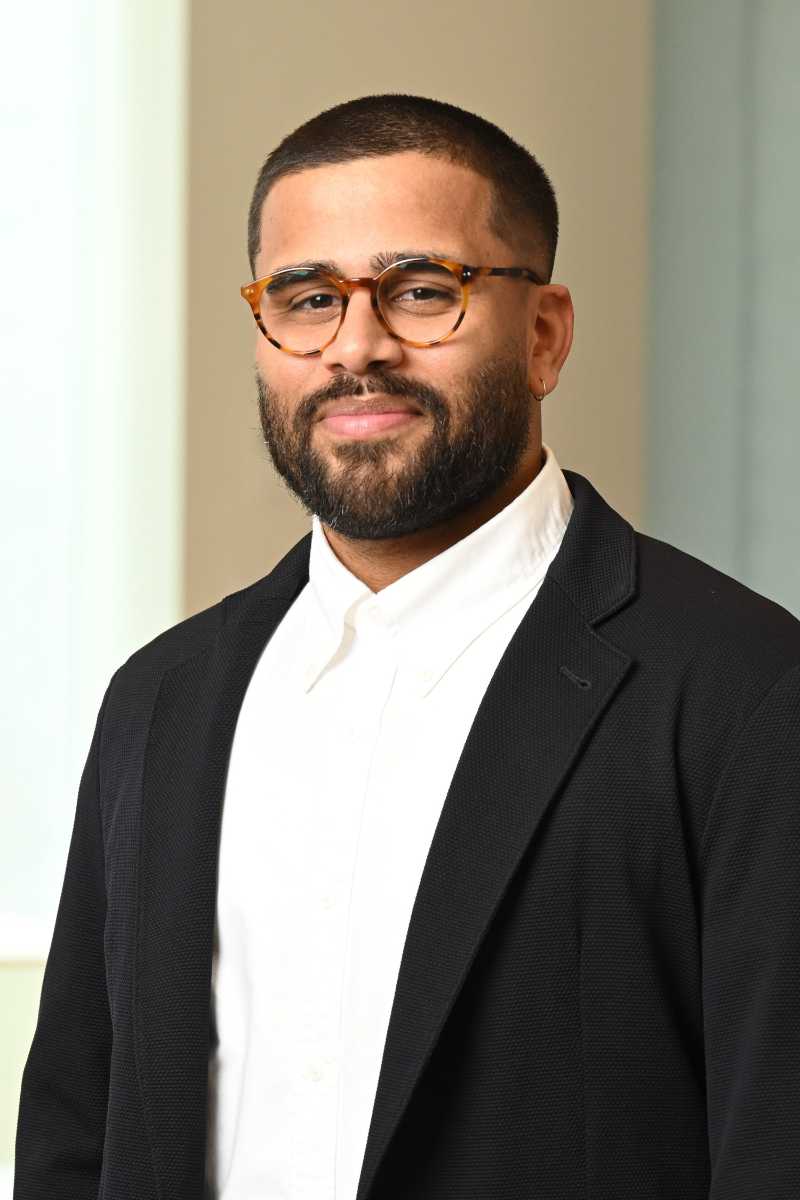 A portrait of Stephane Andrade, a person with short black hair and beard and a black suit coat.