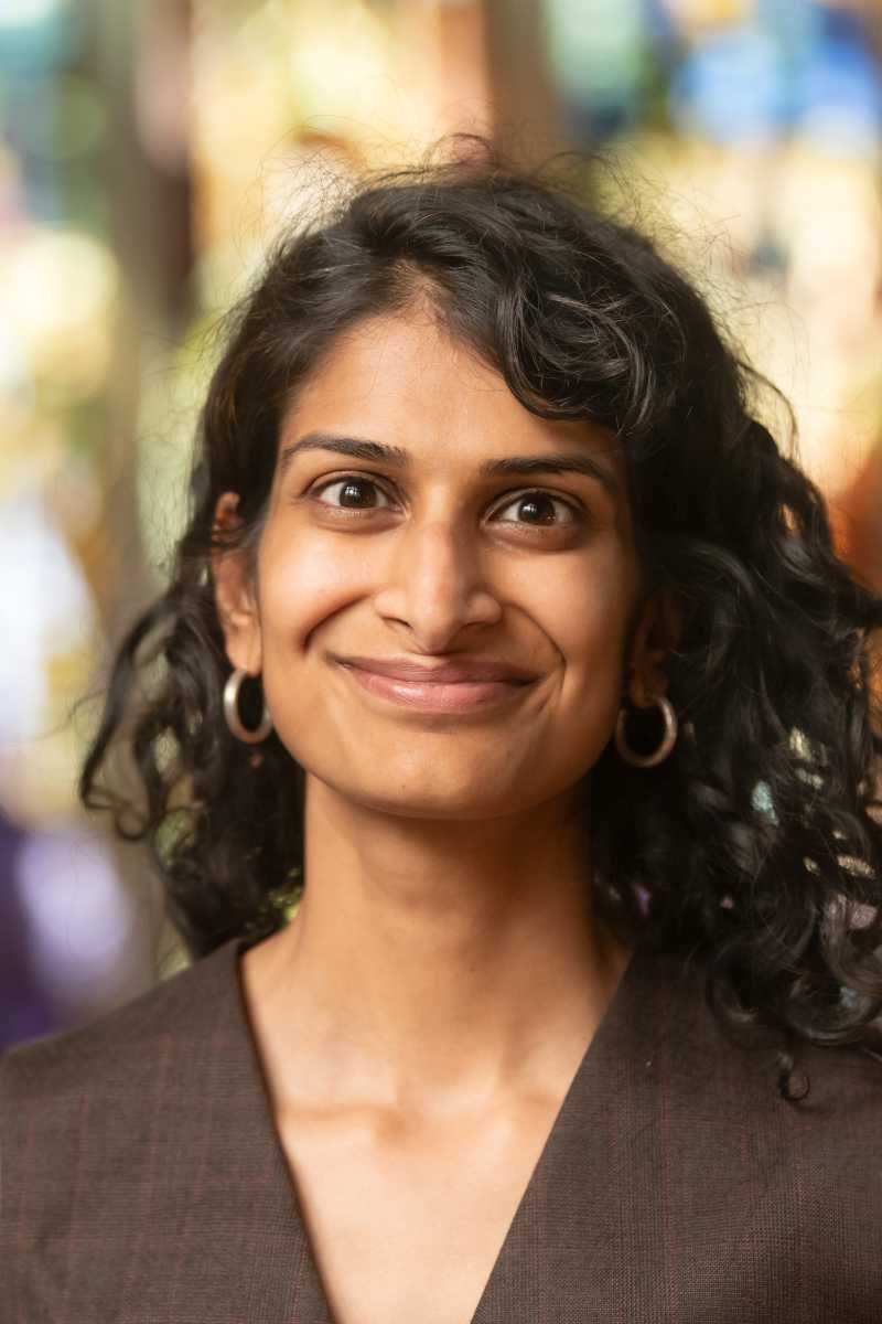 A portrait of Shivani Radhakrishnan, a person with long black hair and a brown shirt.