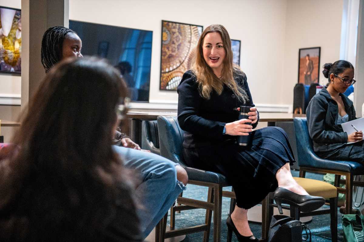 Dr. Michelle Monje ’98, a person with long blond hair and a dark dress, sits in a room talking to some other people.