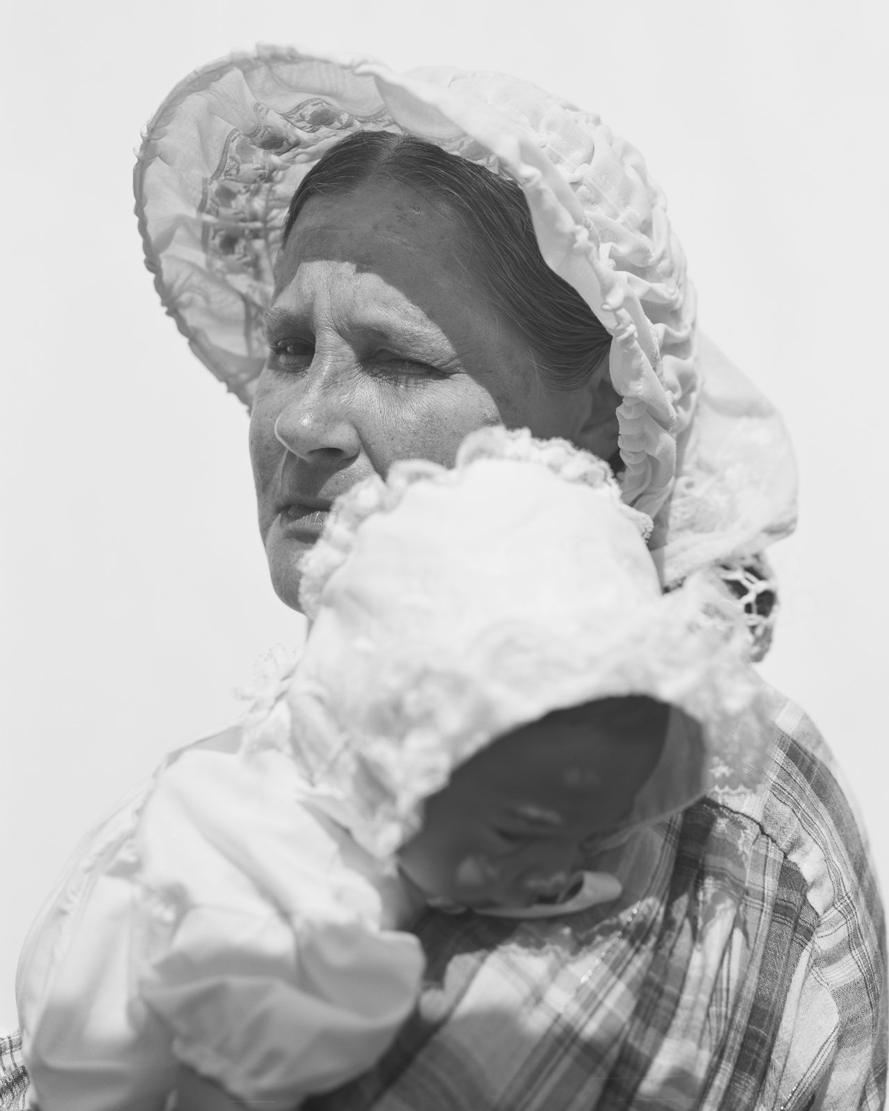 A close-up photograph of a woman holding a small child. They wear historical clothing.