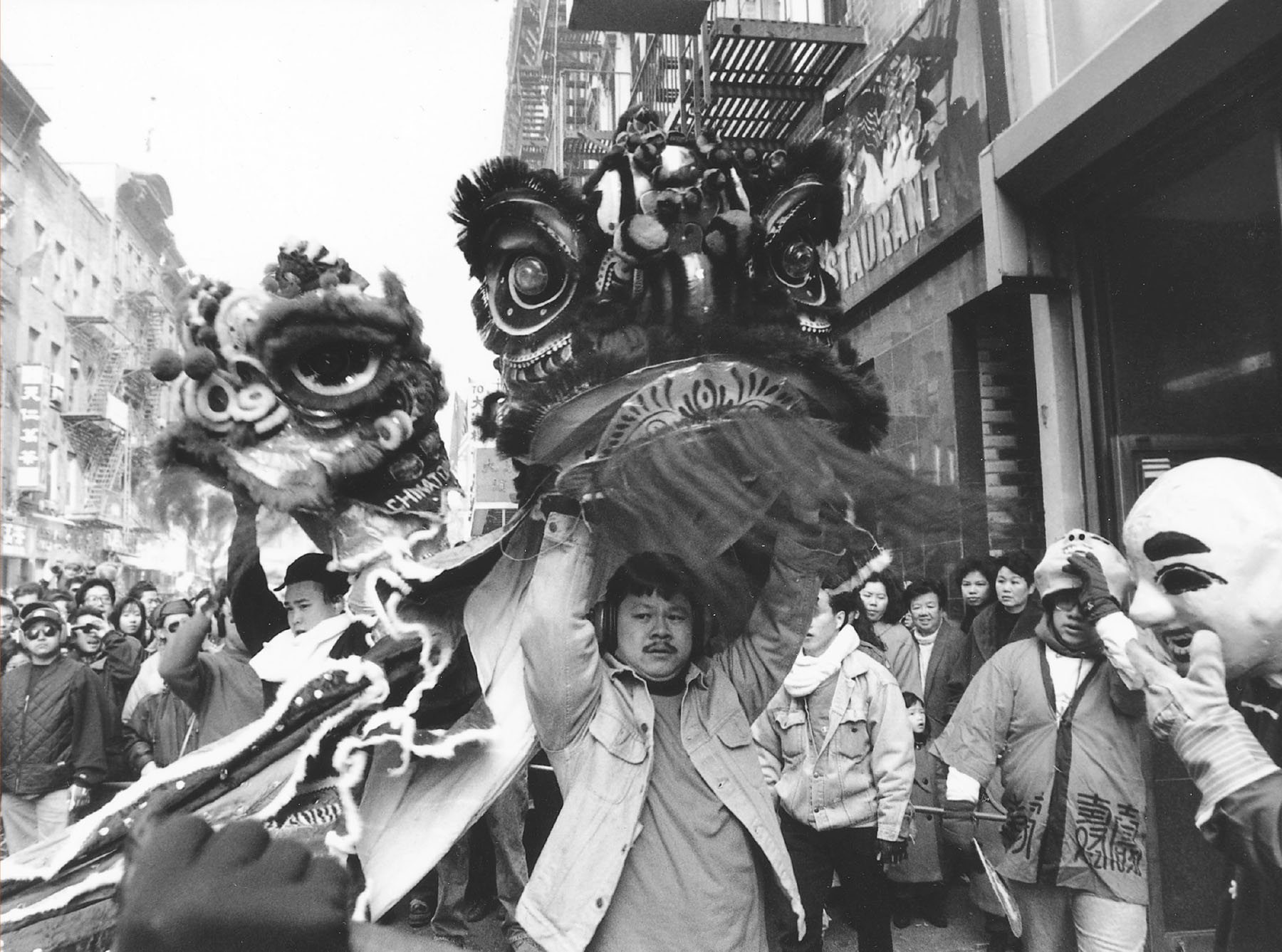 A black and white photo of a bustling city street during a parade with a Chinese Dragon being carried.