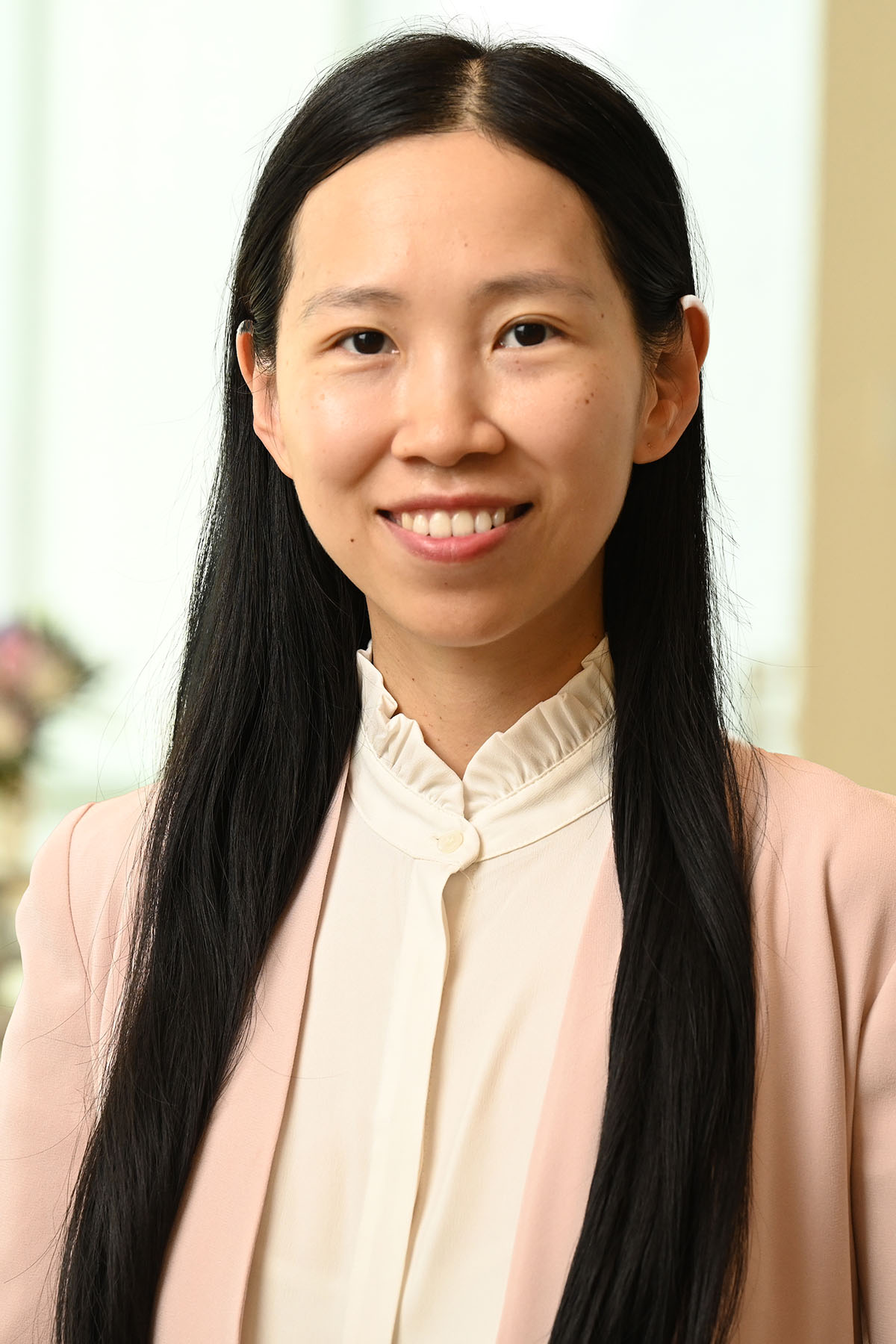 Person with long dark hair wearing a pink sweater over a white shirt with a ruffled collar.