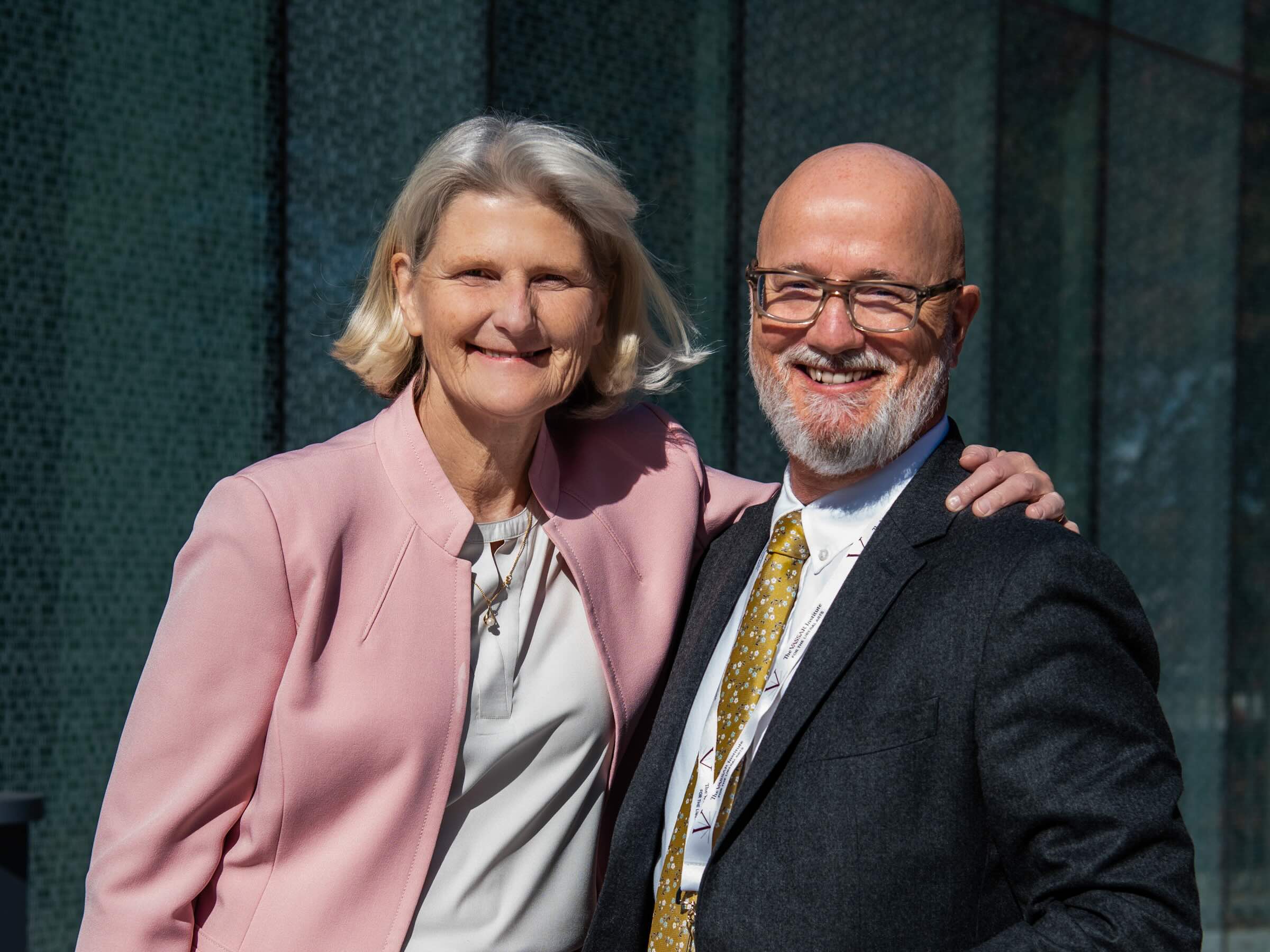 Two smiling people arm in arm in bright sunlight.