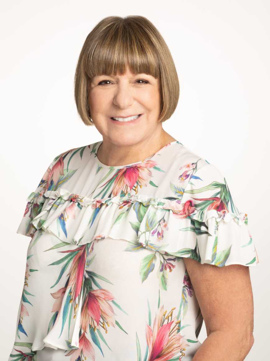 A portrait of Carol Ostrow ’77, a person with shoulder-length brown hair in bangs and a white floral shirt.