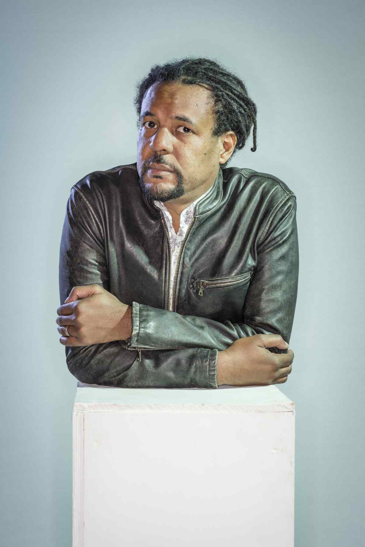 Colson Whitehead, a person with dark hair and a dark mustache, looks at the viewer.