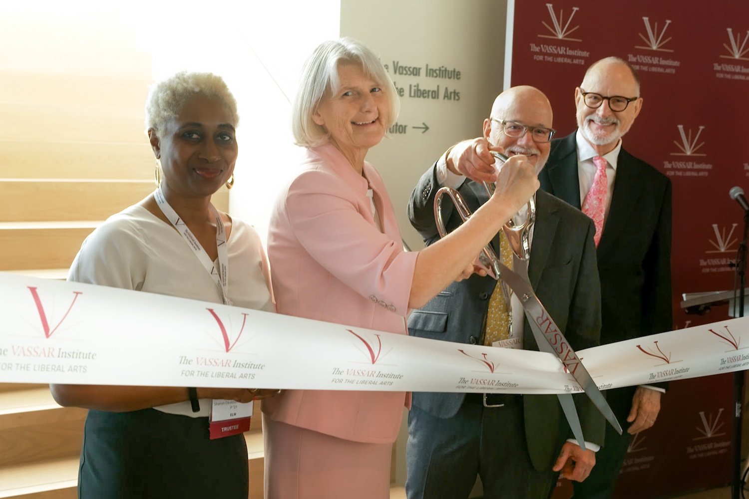 Four of smiling people cutting a ribbon together.