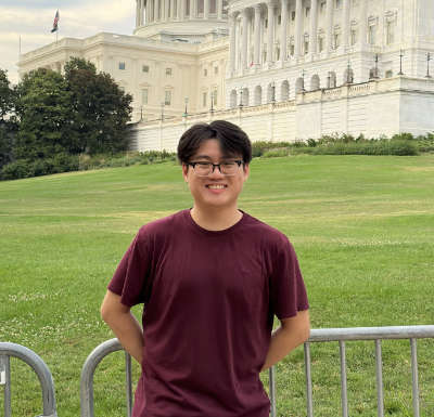 A portrait of Tianyu Xiong ’25, a person with short black hair, glasses, and a brown shirt.