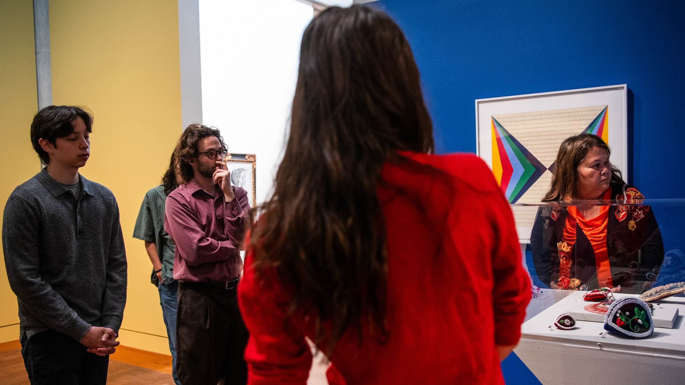 People standing in an art gallery gathered around a glass case and look to their left.