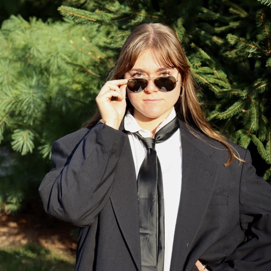 A portrait of Abby Rice, a person with long brown hair, a dark jacket, and sunglasses.