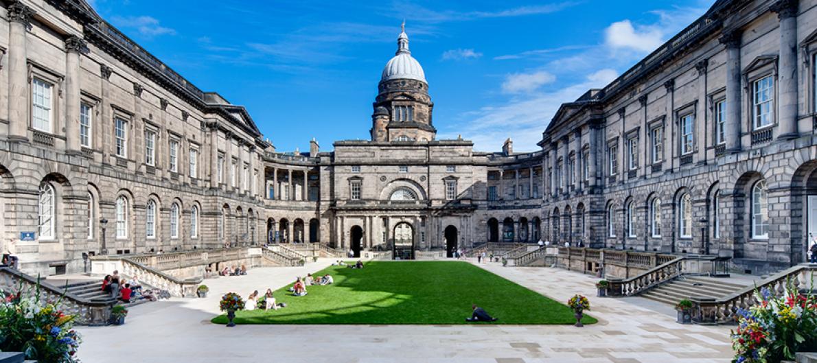 Grey official looking buildings with a capital architecture feature in the background surrounding a small green lawn.