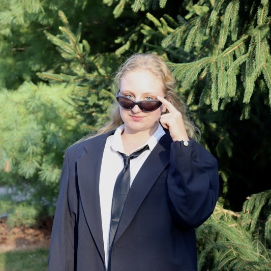 A portrait of Camille Jannuzi, a person with long blonde hair, sunglasses, and a black coat.