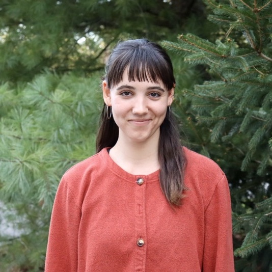 A portrait of Cecilia Kittross, a person with long dark brown hair and an orange shirt.