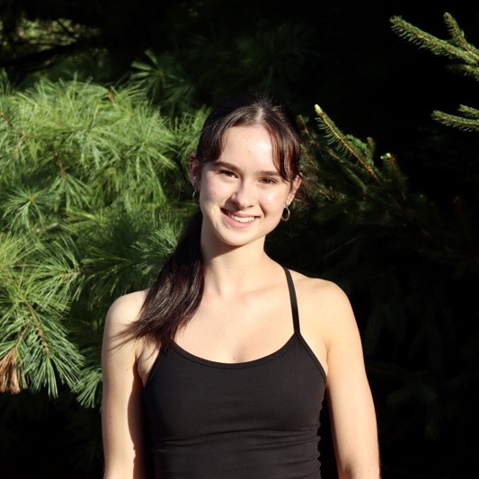 A portrait of Fiora Hogan, a person with long dark brown hair and a black tank top.