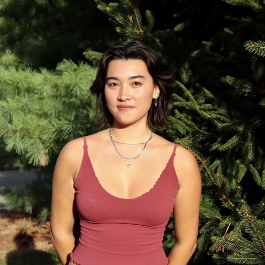 A portrait of Hana Colley, a person with long dark brown hair and a red tank top.