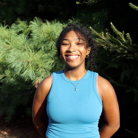 A portrait of Jayla Anderson, a person with long black curly hair and a blue shirt.