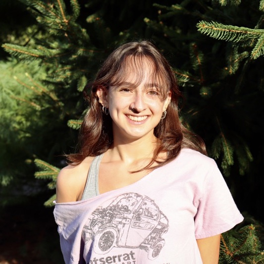 A portrait of Madeline Hsiao, a person with long brown hair and a lavender shirt that says "Montserrat".