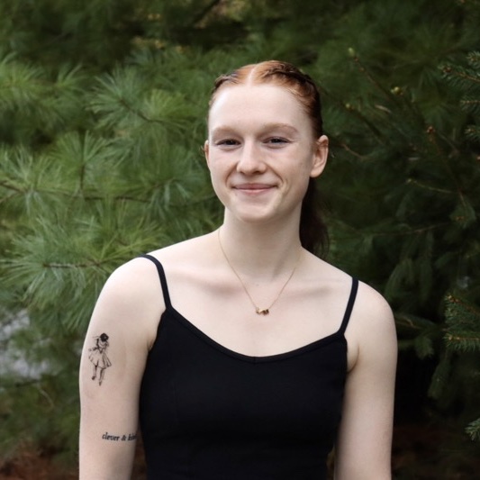 A portrait of Meg Matchett, a person with long red hair and a black tank top.