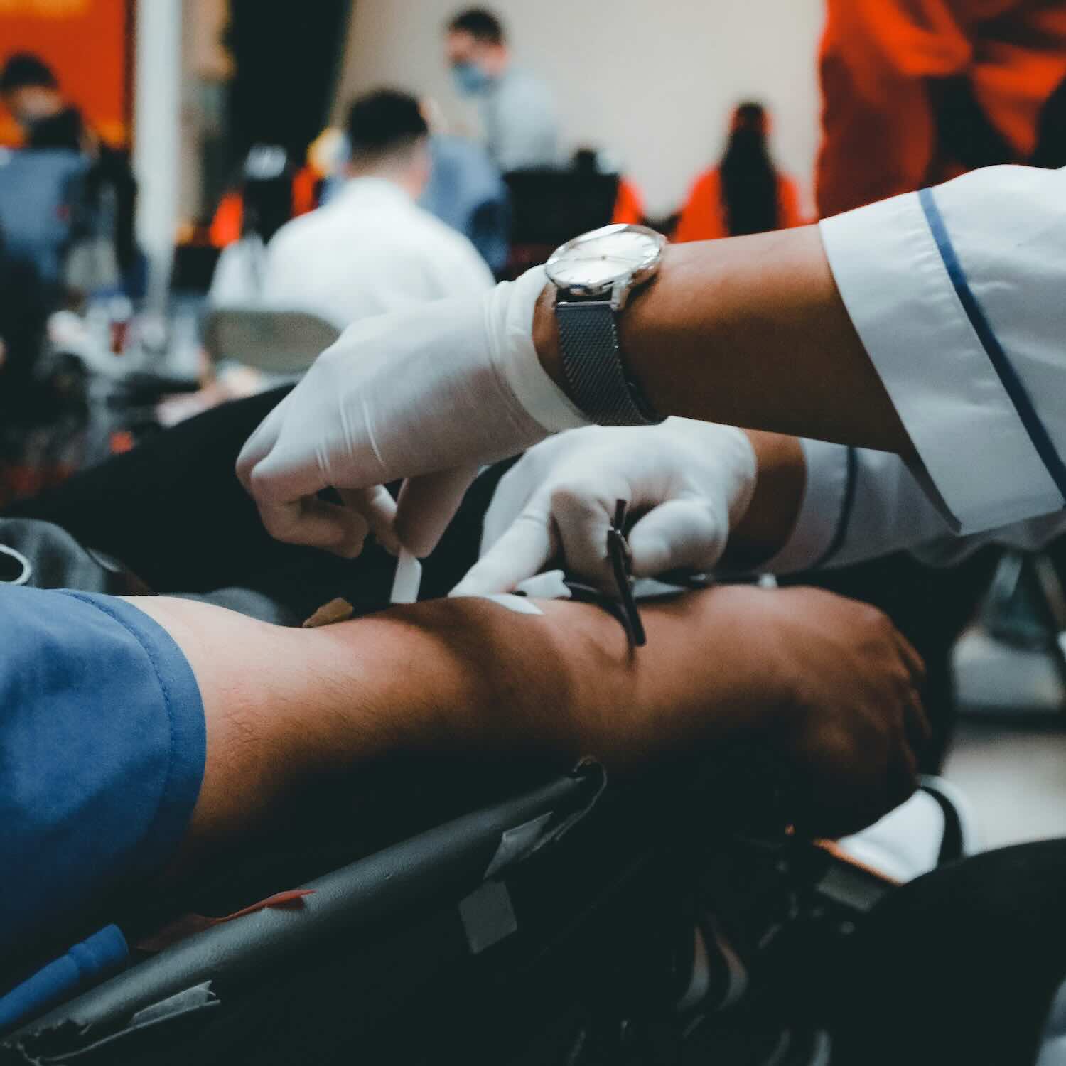 Gloved hands applying a bandage to an arm after giving blood.