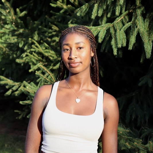 A portrait of Olivia Sparks, a person with long braided black hair and a white tank top.