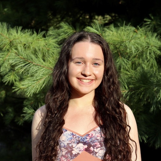 A portrait of Tara Sweeney, a person with long brown hair and a floral shirt.