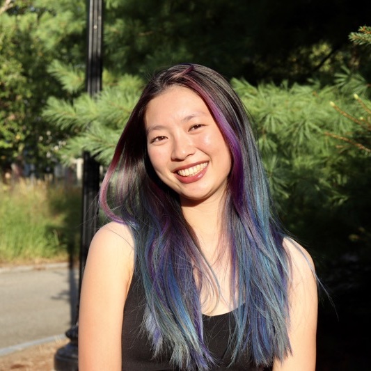 A portrait of Zoë LaCheen-Fine, a person with long black rainbow-tinted hair and a black tank top.