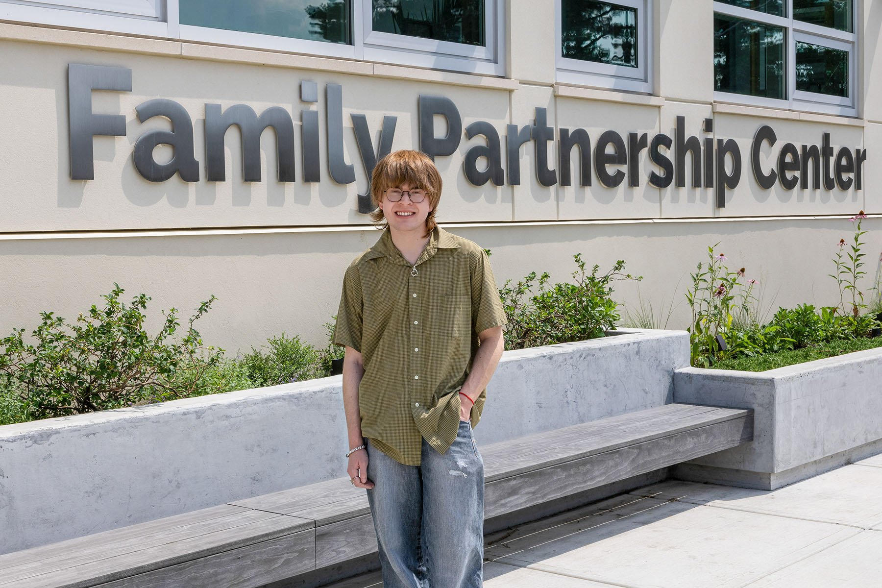 Person standing in front of a large concrete building/wall with the words "Family Partnership Center" in the background.