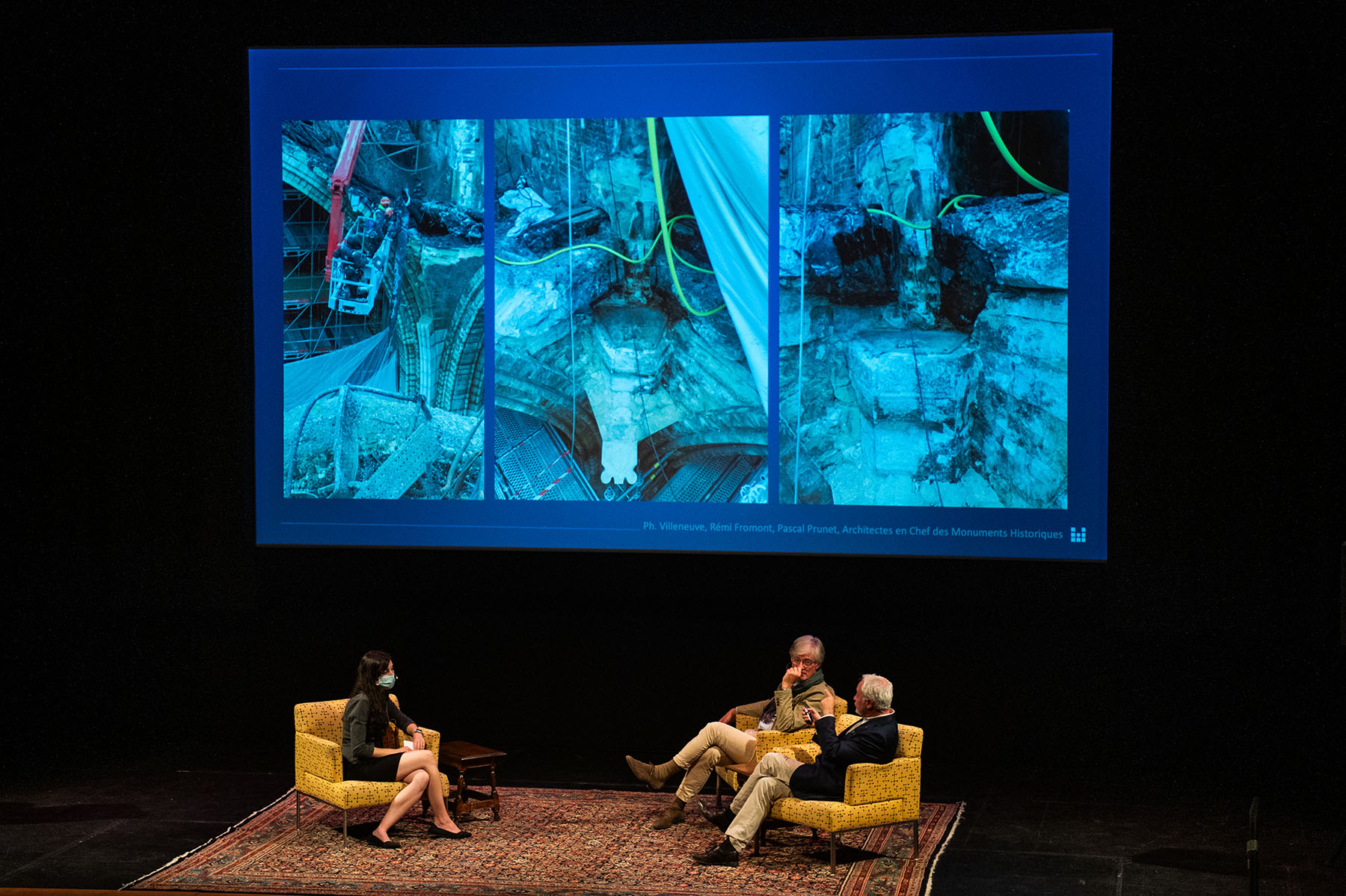 Three people sitting with a projected image of the restoration project of the Notre-Dame in the background.