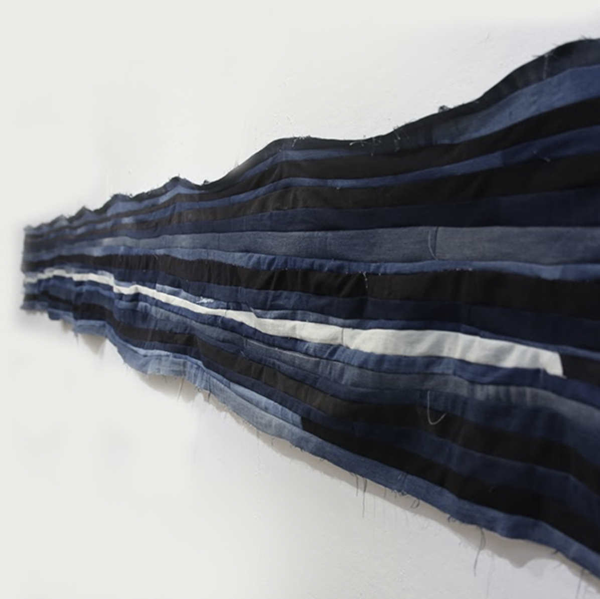 An abstract artwork made from cloth and denim. The artwork is flowing blue, gray, and black lines.