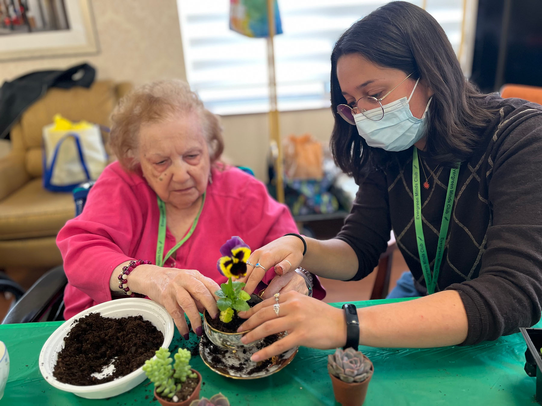 Two people at a table working together to plant a seedling.