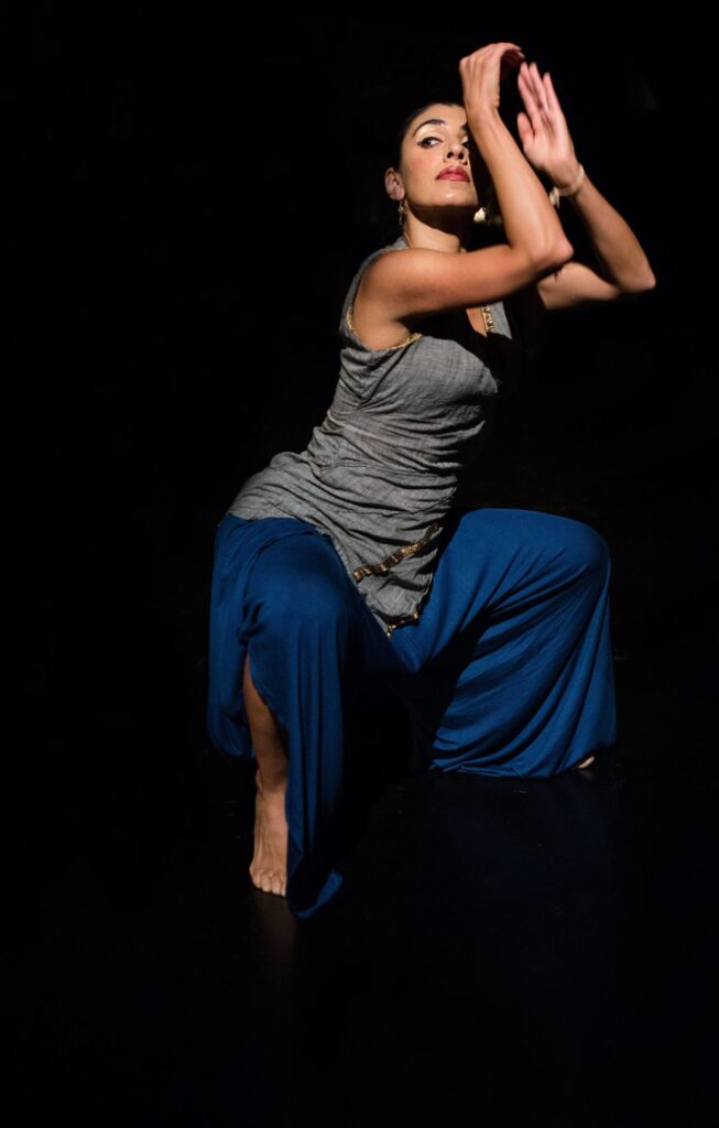 A person in a dancing pose on on a darkened stage.