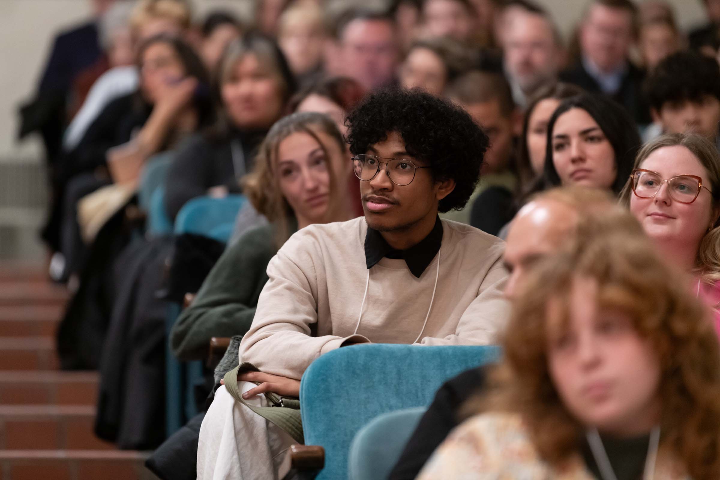 A large group of people sitting in a lecture hall, watching intently.