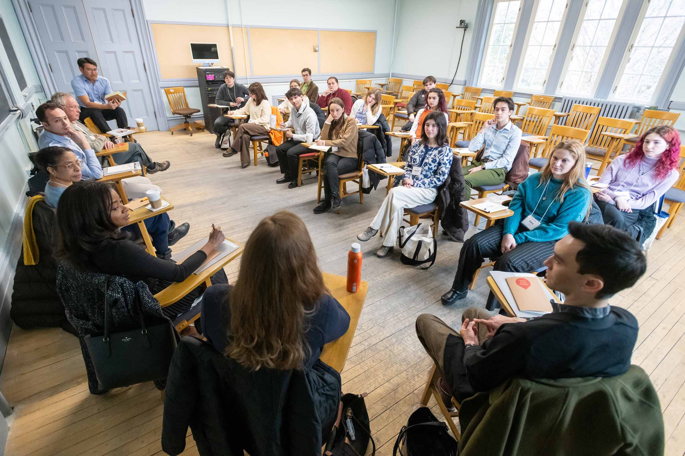 People sitting in wooden, student desks in two lines facing each other.