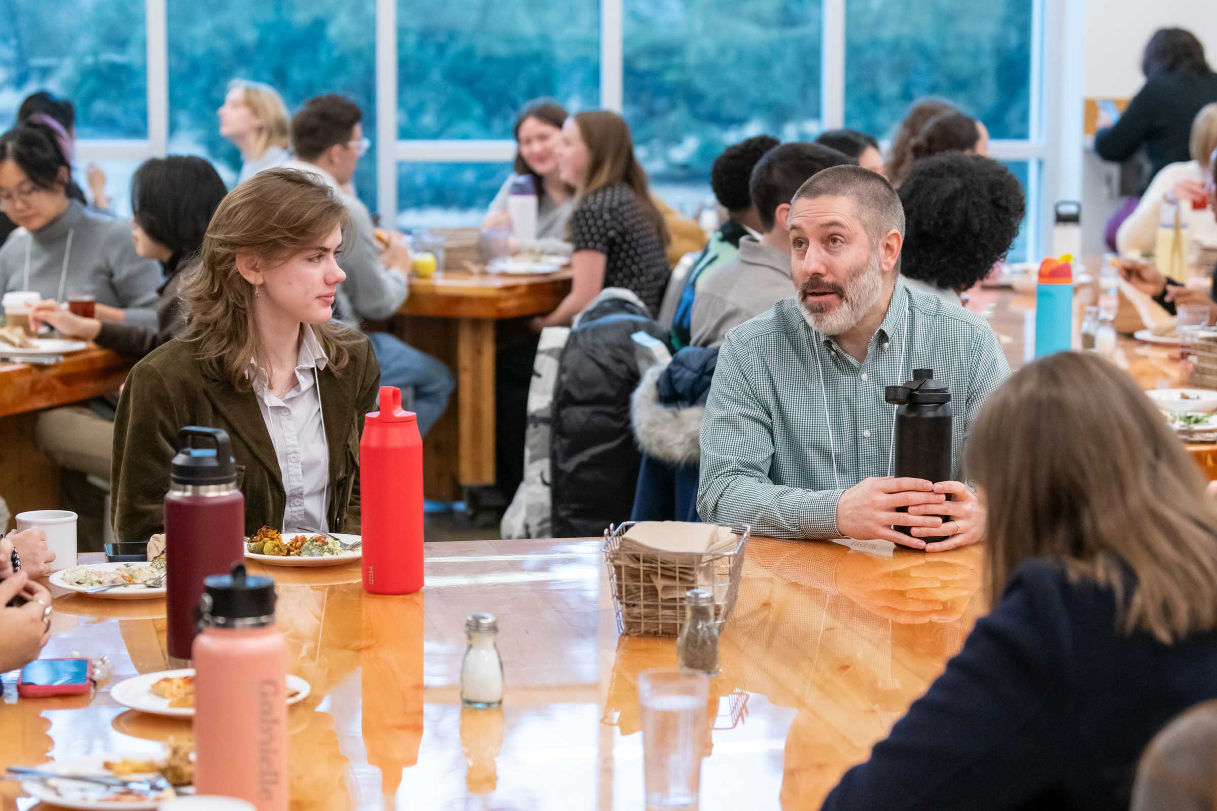 Two seated people at a table with food and drink talking.