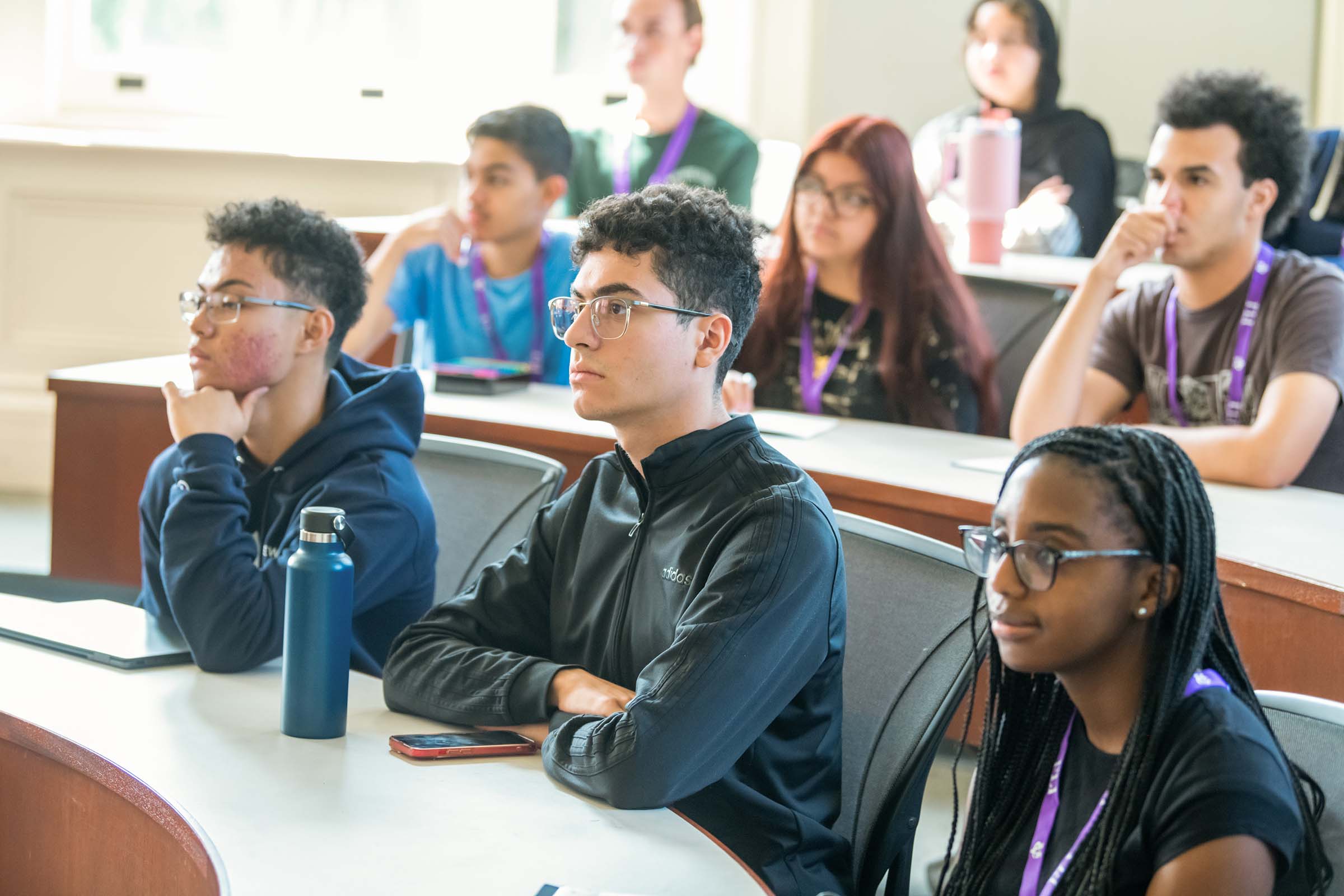 A section of three rows of people sitting at lecture desks intently watching.