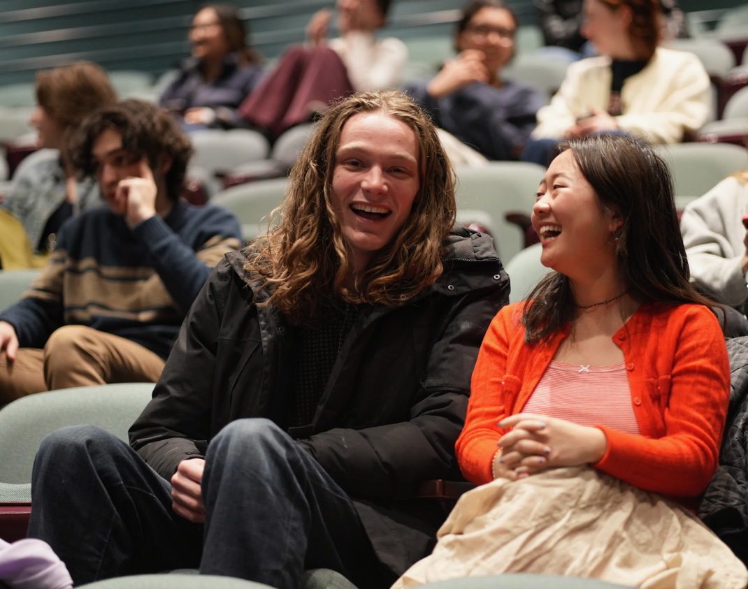 Interns Garrett Schmid ’25 and Tori Kim ’25 sitting next to each other in auditorium seats.