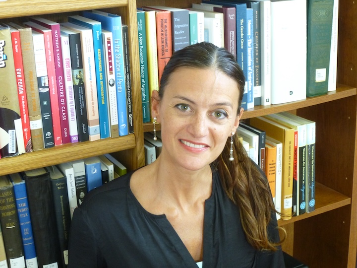 A portrait photo of Natalia Milanesio  posing in front of a bookshelf.