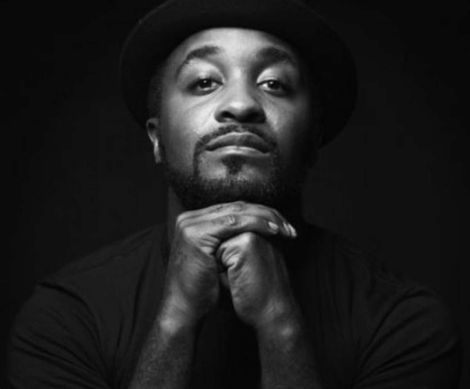 A black and white portrait of Darrell Moultrie, a person with black facial hair and hands folded in front of them.