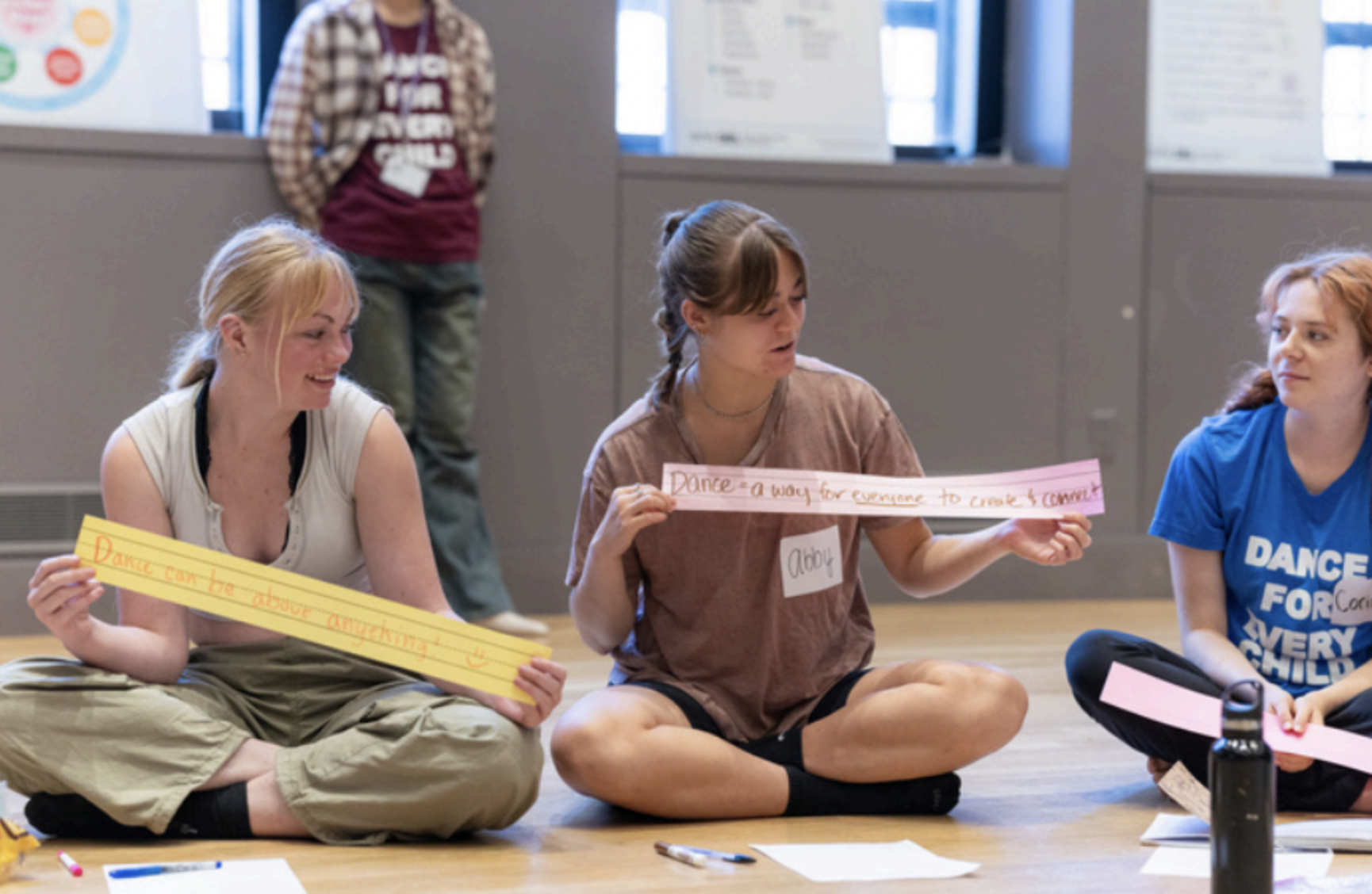 Three people sit cross-legged in a room holding pieces of paper.