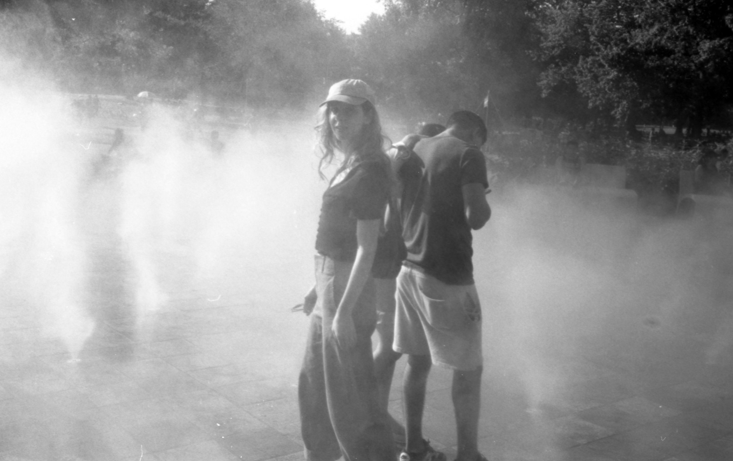 Black and white image of two people standing outside, back to back, with fog all around them.