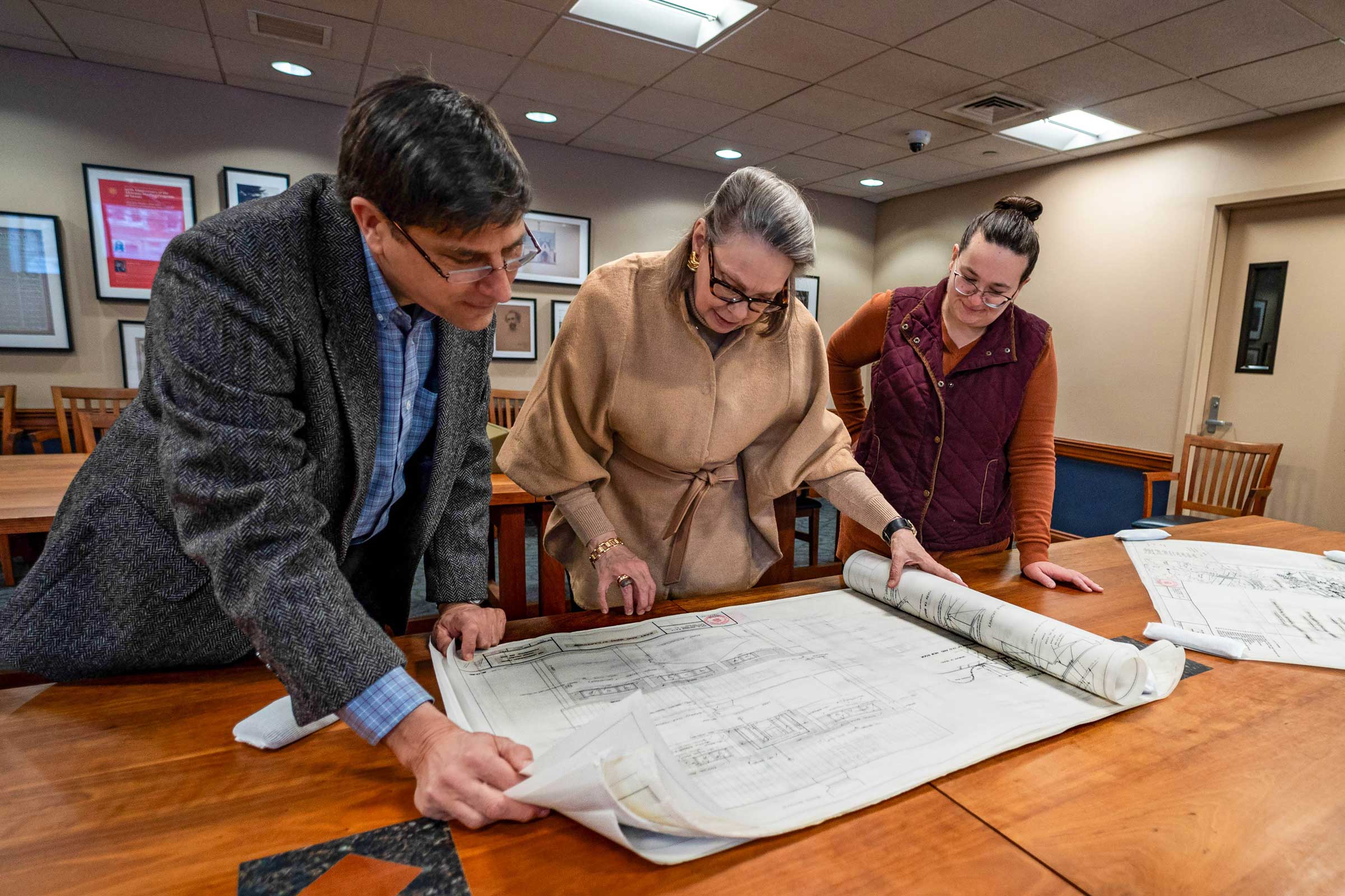 Three people standing over a table looking at paper architectural plans.